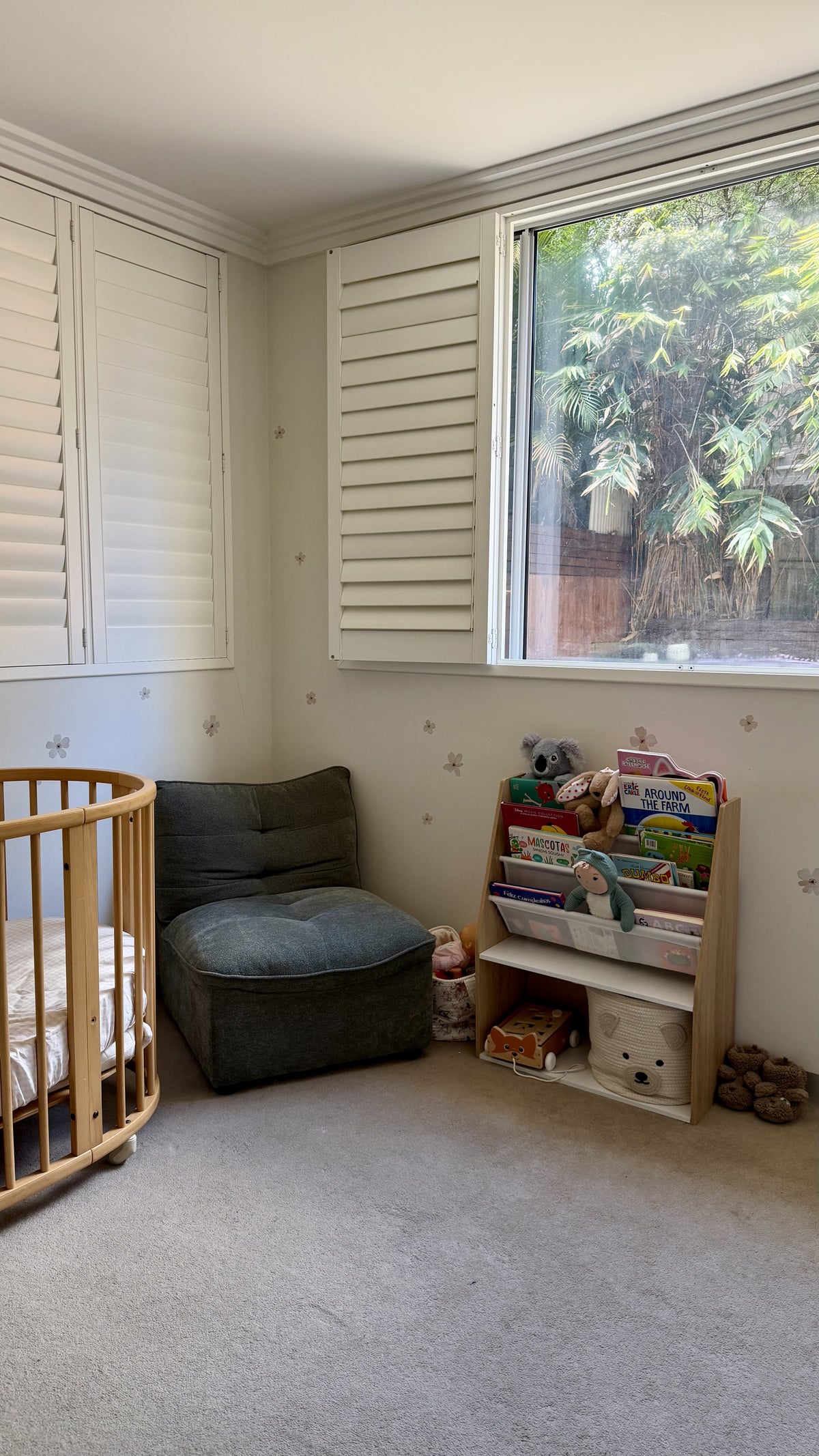 Real nursery with Ivory Bloom removable flower wall stickers on cream walls, featuring a wooden cot, cosy chair and children's bookshelf.
